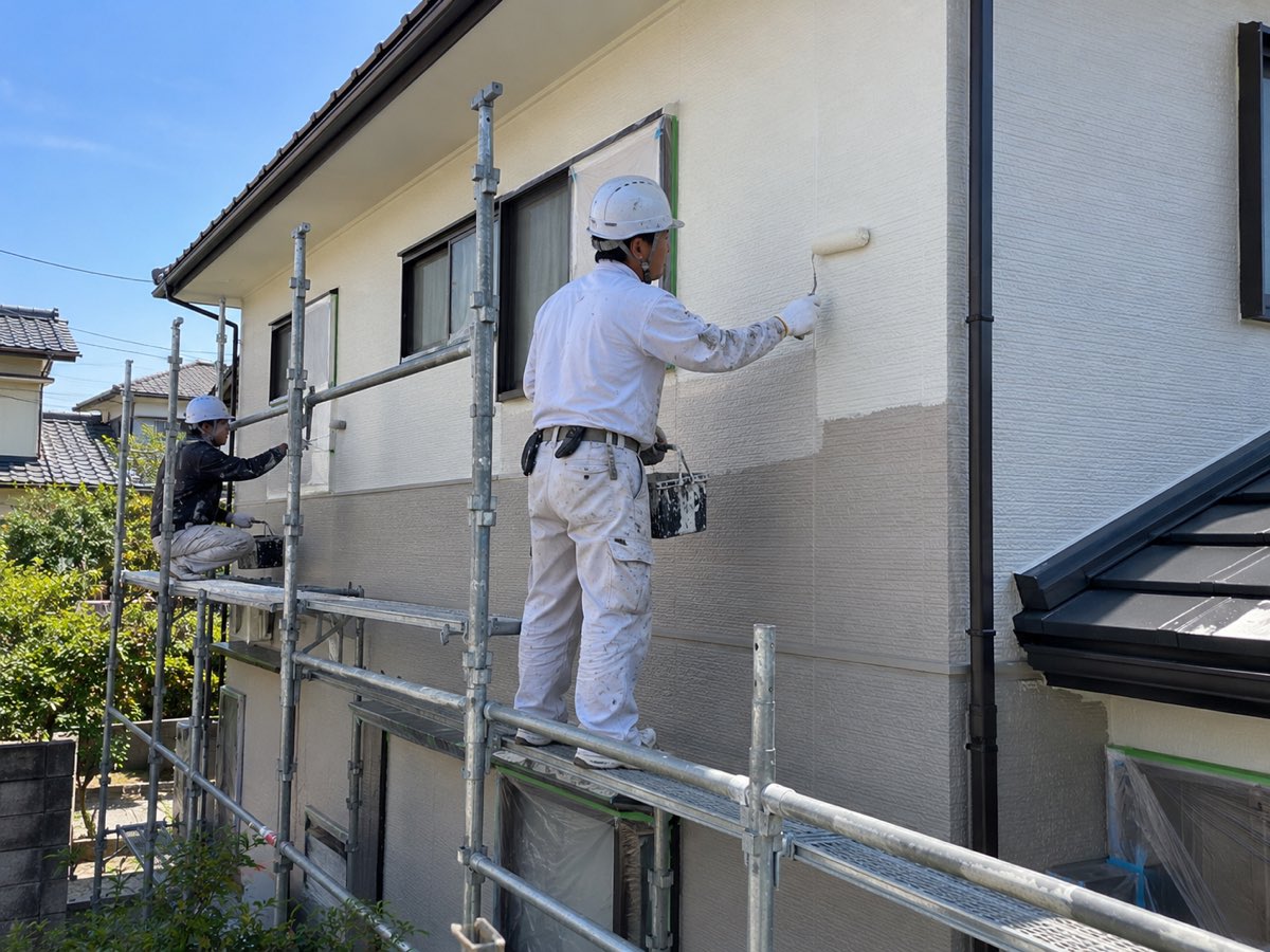 足場の上で住宅の外壁をローラーで塗装している様子